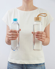 Image showing Two bottles of glass and plastic of clean fresh water in a woman\'s hands.