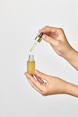 Image showing Bottle and pipet of medical cannabis CBD oil in hands against a light grey background.