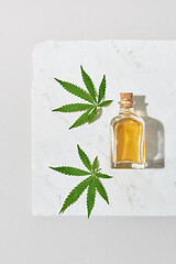 Image showing Medical marijuana oil and green cannabis leaves on a light grey marble background.