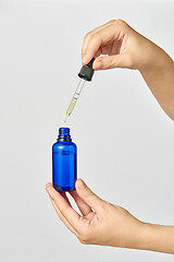 Image showing Female\'s hand holds a pipet of natural extract CBD oil against a light grey background.