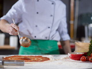 Image showing Chef smearing pizza dough with ketchup