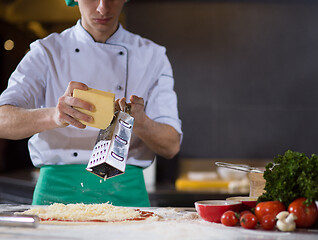 Image showing chef sprinkling cheese over fresh pizza dough