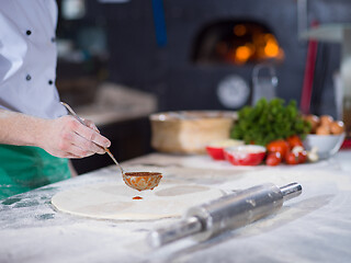 Image showing Chef smearing pizza dough with ketchup