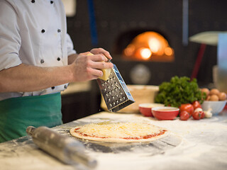 Image showing chef sprinkling cheese over fresh pizza dough
