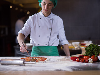 Image showing Chef smearing pizza dough with ketchup