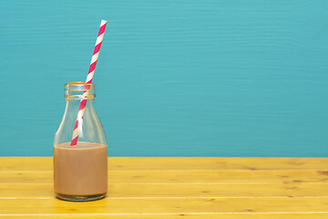 Image showing Glass bottle half full with chocolate milkshake with paper straw