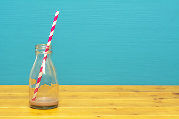 Image showing Glass bottle with dregs of chocolate milkshake and a straw