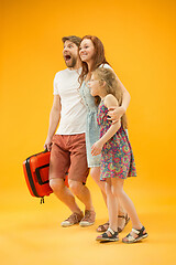 Image showing Happy parents with daughter and suitcase at studio isolated on yellow background