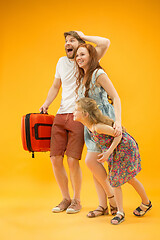 Image showing Happy parents with daughter and suitcase at studio isolated on yellow background