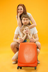 Image showing Happy parents with daughter and suitcase at studio isolated on yellow background