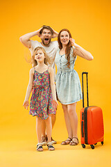 Image showing Happy parents with daughter and suitcase at studio isolated on yellow background