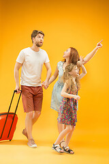 Image showing Happy parents with daughter and suitcase at studio isolated on yellow background