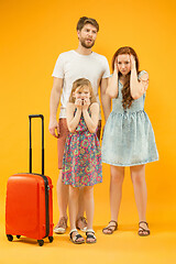 Image showing Sad parents with daughter and suitcase at studio isolated on yellow background