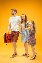 Image showing Happy parents with daughter and suitcase at studio isolated on yellow background