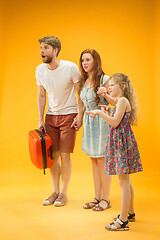 Image showing Sad parents with daughter and suitcase at studio isolated on yellow background