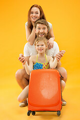 Image showing Happy parents with daughter and suitcase at studio isolated on yellow background