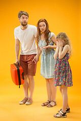 Image showing Sad parents with daughter and suitcase at studio isolated on yellow background