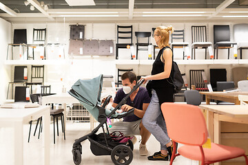 Image showing Young couple with newborn in stroller shopping at retail furniture and home accessories store wearing protective medical face mask to prevent spreading of corona virus when shops reopen.