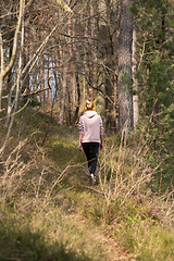 Image showing Rear view of active sporty woman listening to the music while running in autumn fall forest. Female runner training outdoor. Healthy lifestyle image of young caucasian woman jogging outside