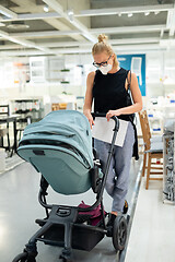 Image showing Young mom with newborn in stroller shopping at retail furniture and home accessories store wearing protective medical face mask to prevent spreading of corona virus. New normal during covid epidemic