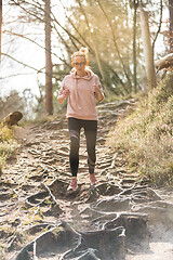 Image showing Active sporty woman listening to the music while running in autumn fall forest. Female runner training outdoor. Healthy lifestyle image of young caucasian woman jogging outside