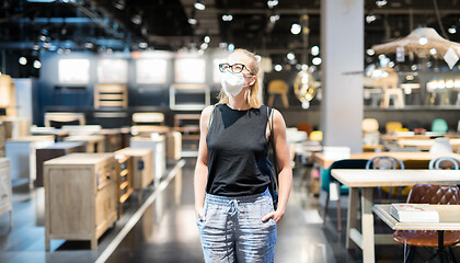 Image showing New normal during covid epidemic. Caucasian woman shopping at retail furniture and home accessories store wearing protective medical face mask to prevent spreading of corona virus