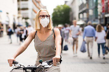 Image showing Woman riding bicycle on city street wearing medical face mask in public to prevent spreading of corona virus. New normal during covid epidemic.