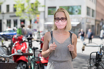 Image showing Portrait of casual yound woman walking on the street wearing protective mask as protection against covid-19 virus. Incidental people on the background