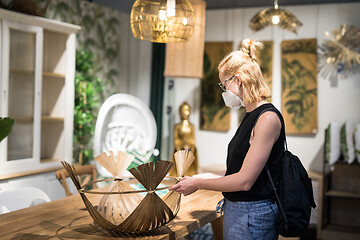 Image showing New normal during covid epidemic. Caucasian woman shopping at retail furniture and home accessories store wearing protective medical face mask to prevent spreading of corona virus