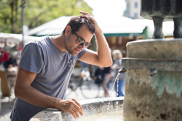 Image showing Young casual cucasian man refreshing himself with water from public city fountain on a hot summer day