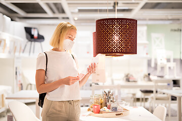 Image showing New normal during covid epidemic. Caucasian woman shopping at retail furniture and home accessories store wearing protective medical face mask to prevent spreading of corona virus