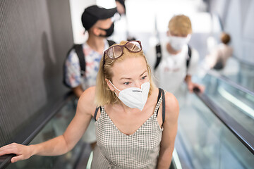 Image showing Portrait of casual yound woman uses escalators in the department store wearing protective mask as protection against covid-19 virus. Incidental people on the background