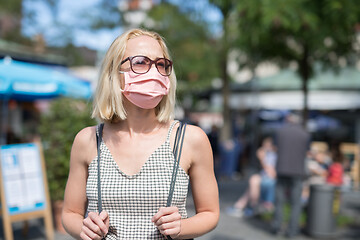 Image showing Portrait of casual yound woman walking on the street wearing protective mask as protection against covid-19 virus. Incidental people on the background