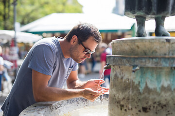 Image showing Thirsty young casual cucasian man drinking water from public city fountain on a hot summer day