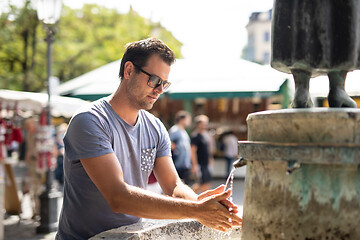 Image showing Young casual cucasian man washing hands with water from public city fountain on a hot summer day