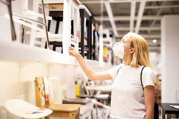 Image showing New normal during covid epidemic. Caucasian woman shopping at retail furniture and home accessories store wearing protective medical face mask to prevent spreading of corona virus