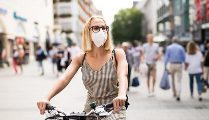 Image showing Woman riding bicycle on city street wearing medical face mask in public to prevent spreading of corona virus. New normal during covid epidemic.