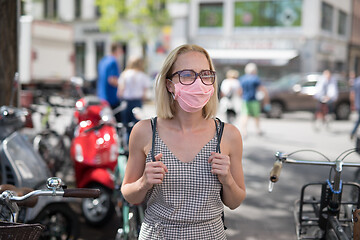 Image showing Portrait of casual yound woman walking on the street wearing protective mask as protection against covid-19 virus. Incidental people on the background