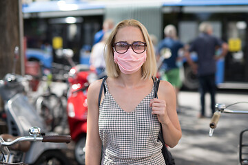 Image showing Portrait of casual yound woman walking on the street wearing protective mask as protection against covid-19 virus. Incidental people on the background