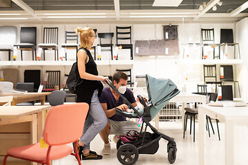 Image showing Young couple with newborn in stroller shopping at retail furniture and home accessories store wearing protective medical face mask to prevent spreading of corona virus when shops reopen.