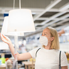 Image showing New normal during covid epidemic. Caucasian woman shopping at retail furniture and home accessories store wearing protective medical face mask to prevent spreading of corona virus