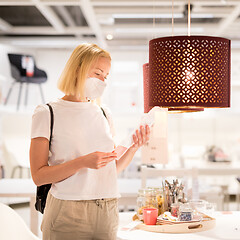 Image showing New normal during covid epidemic. Caucasian woman shopping at retail furniture and home accessories store wearing protective medical face mask to prevent spreading of corona virus