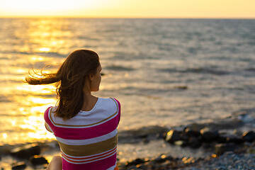 Image showing A girl sits in the evening at sunset on the seashore, view from the back