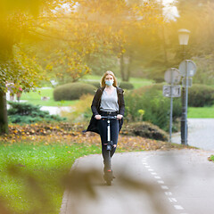 Image showing Casual caucasian teenager wearing protective face mask riding urban electric scooter in city park during covid pandemic. Urban mobility concept