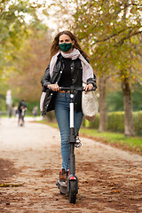 Image showing Casual caucasian teenager wearing protective face mask riding urban electric scooter in city park during covid pandemic. Urban mobility concept