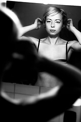 Image showing Woman getting ready for work doing morning makeup routine applying make up and doing her hair in front of bathroom mirror at home. Black and white image