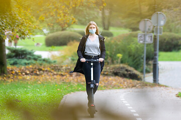 Image showing Casual caucasian teenager wearing protective face mask riding urban electric scooter in city park during covid pandemic. Urban mobility concept