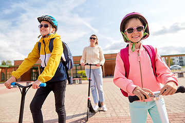 Image showing happy school children with mother riding scooters