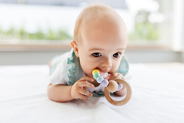 Image showing baby girl on white blanket chewing wooden rattle