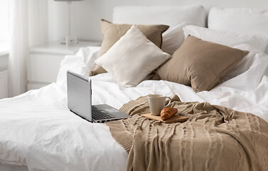 Image showing laptop, cup of coffee and croissant on bed at home